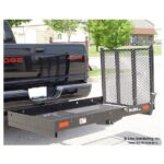 A black pickup truck with a 4x4 logo has a metal cargo carrier attached to the rear. The carrier has a mesh base and side rails and is extended outward from the truck’s hitch. Trees, a lawn, and a house are seen in the background.