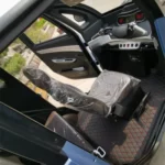 Interior of a small electric vehicle with a single seat, showing protective plastic covers and simple dashboard controls.