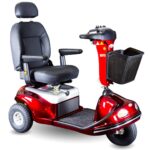 A red mobility scooter with a cushioned black seat and backrest, armrests, a front basket, and three wheels. The handlebar has control buttons, and the scooter features footrests and headlights at the front.