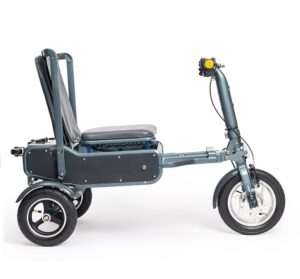 The image features the eFOLDi Explorer Mobility Scooter in a semi-folded state, highlighting its versatility and portability. The scooter has a sleek, dark-colored body with a long wheelbase for stability. It has a padded seat that is partially folded down, along with a tall, flexible backrest. The three-wheeled design includes two smaller rear wheels and a large, spoked front wheel, indicating a design optimized for smooth maneuverability. The handlebar, which extends upward, is equipped with handgrips, a control mechanism, and a prominent yellow flower attached, possibly for visibility or decorative purposes. The overall design of the scooter emphasizes ease of use, comfort, and the ability to compactly fold for transport or storage.