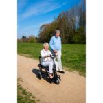 A woman enjoying a sunny day out on an eFOLDi Lite scooter, with a man standing beside her.