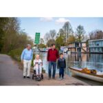 A woman on an eFOLDi Lite scooter accompanied by a family walking along a riverside path.