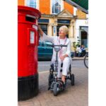 A woman on an eFOLDi Lite scooter posting a letter in a traditional red British postbox.