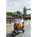 Woman smiling while riding the eFOLDi Explorer scooter on a promenade with the iconic Tower Bridge in the background, demonstrating the scooter's ease of use in a picturesque urban setting.