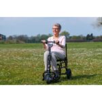 A senior lady enjoying the independence offered by the eFOLDi Lite scooter in a grassy field, portraying the scooter's capability in providing mobility and enjoyment of outdoor activities.