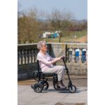 An elderly woman riding the eFOLDi Lite scooter outdoors, with a serene expression, illustrating the scooter's stability and comfort for leisurely rides in open spaces.
