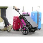 A person partially visible on the left, effortlessly maneuvering the black eFOLDi Lite scooter folded in trolley mode through an airport, with suitcases in the background, highlighting its portability and ease of use.