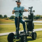 Front view of a person standing on the MIA Four X2 scooter with a golf bag attached on a golf course